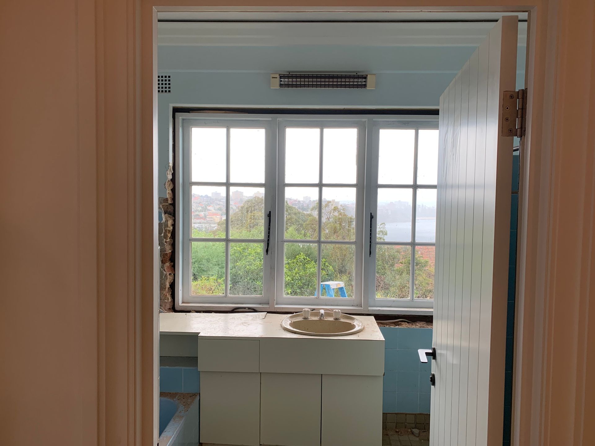 Bathroom renovation in progress, featuring a large window, blue walls, and a white sink base.