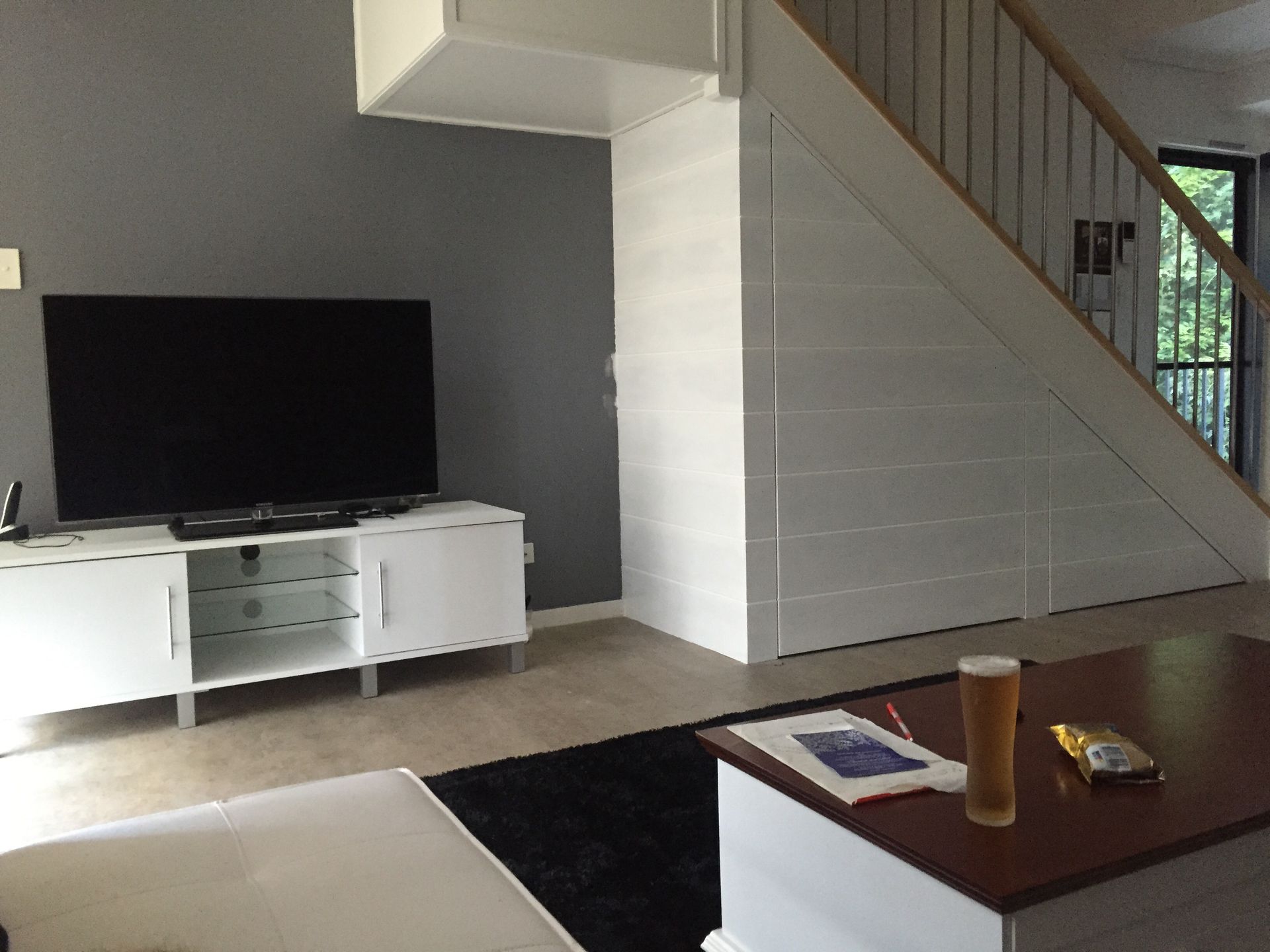 Living room with TV, white cabinet, under-stair storage, and coffee table with drink.