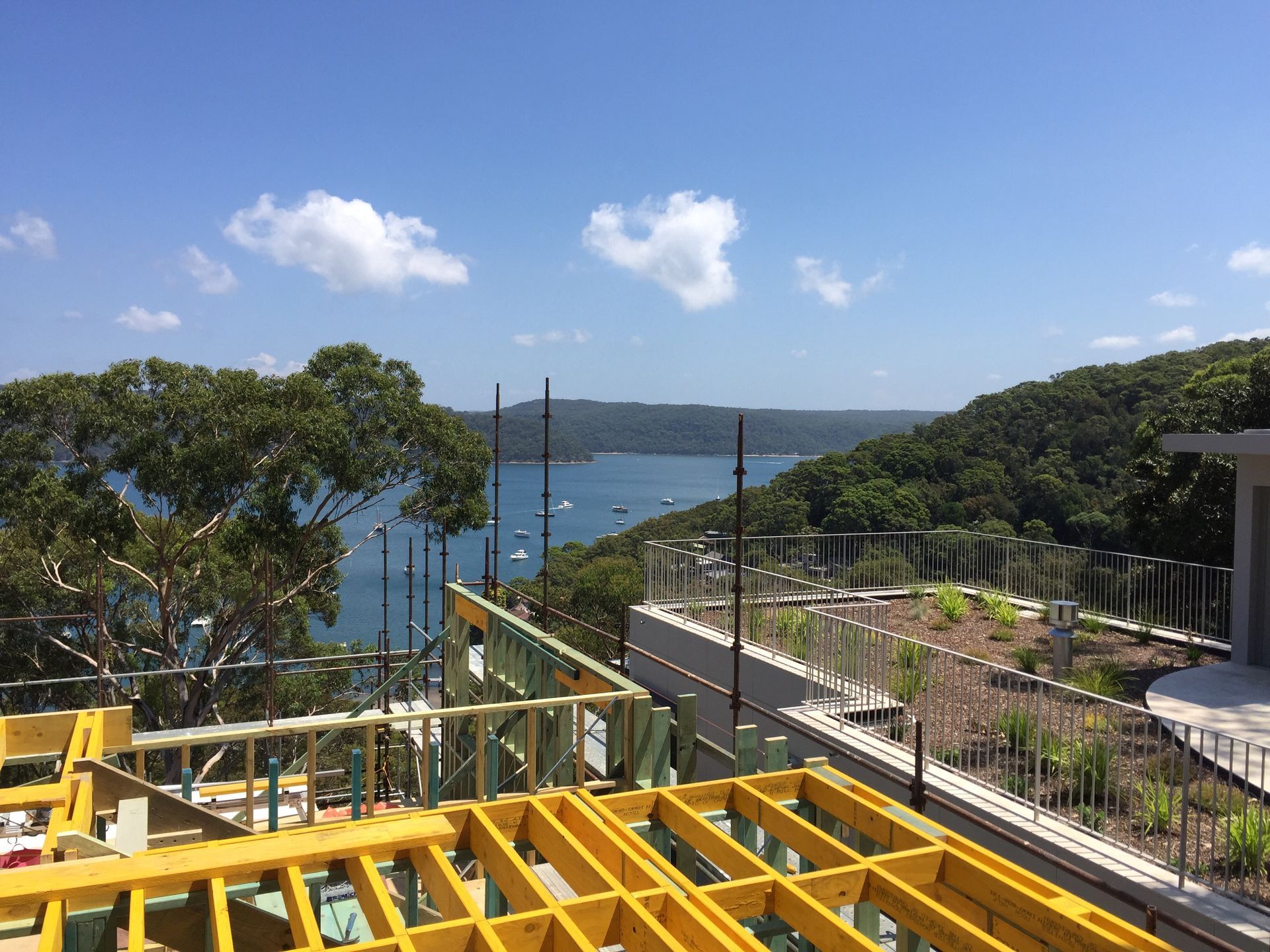 Construction site overlooking a bay with blue water and lush green trees under a partly cloudy sky.