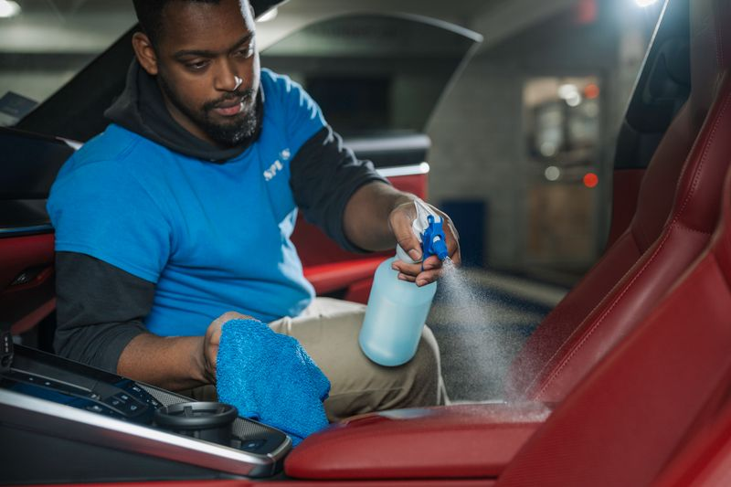 Detailer spraying cleaner onto a red car seat in a garage
