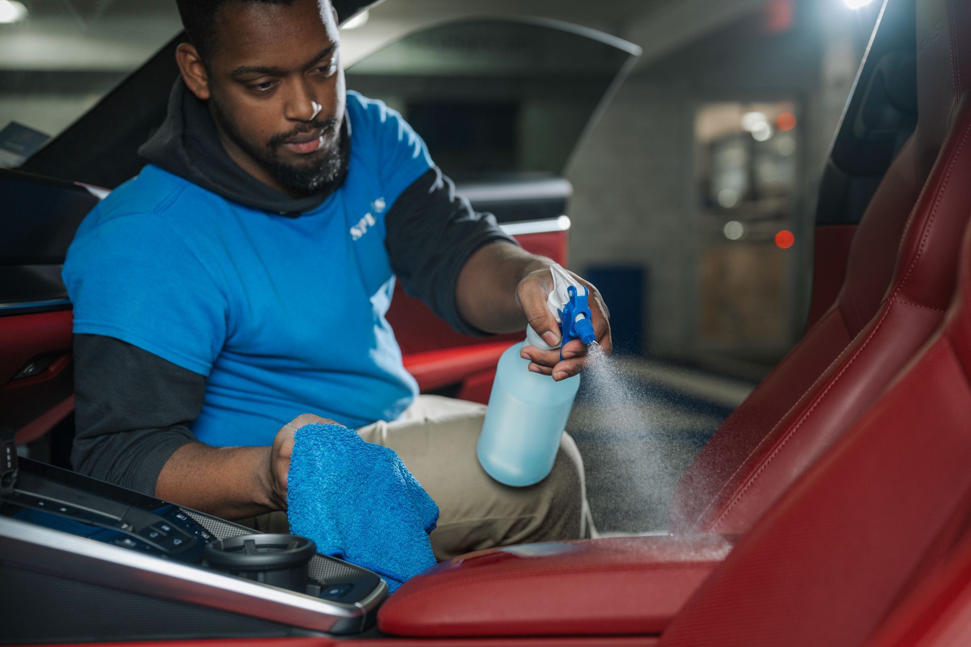 A man is cleaning the interior of a car with a spray bottle.