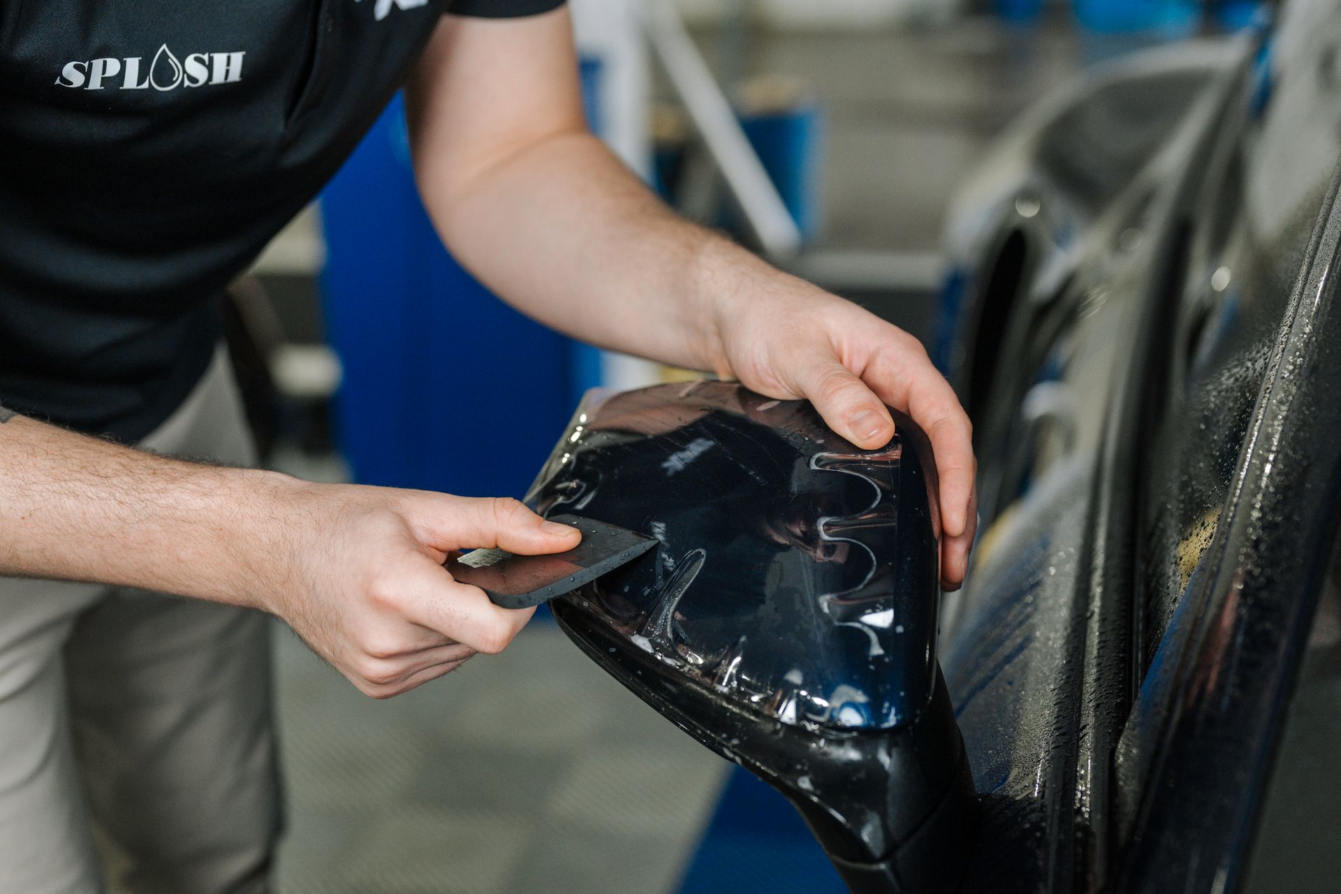 A man is applying a protective film to the side mirror of a car.