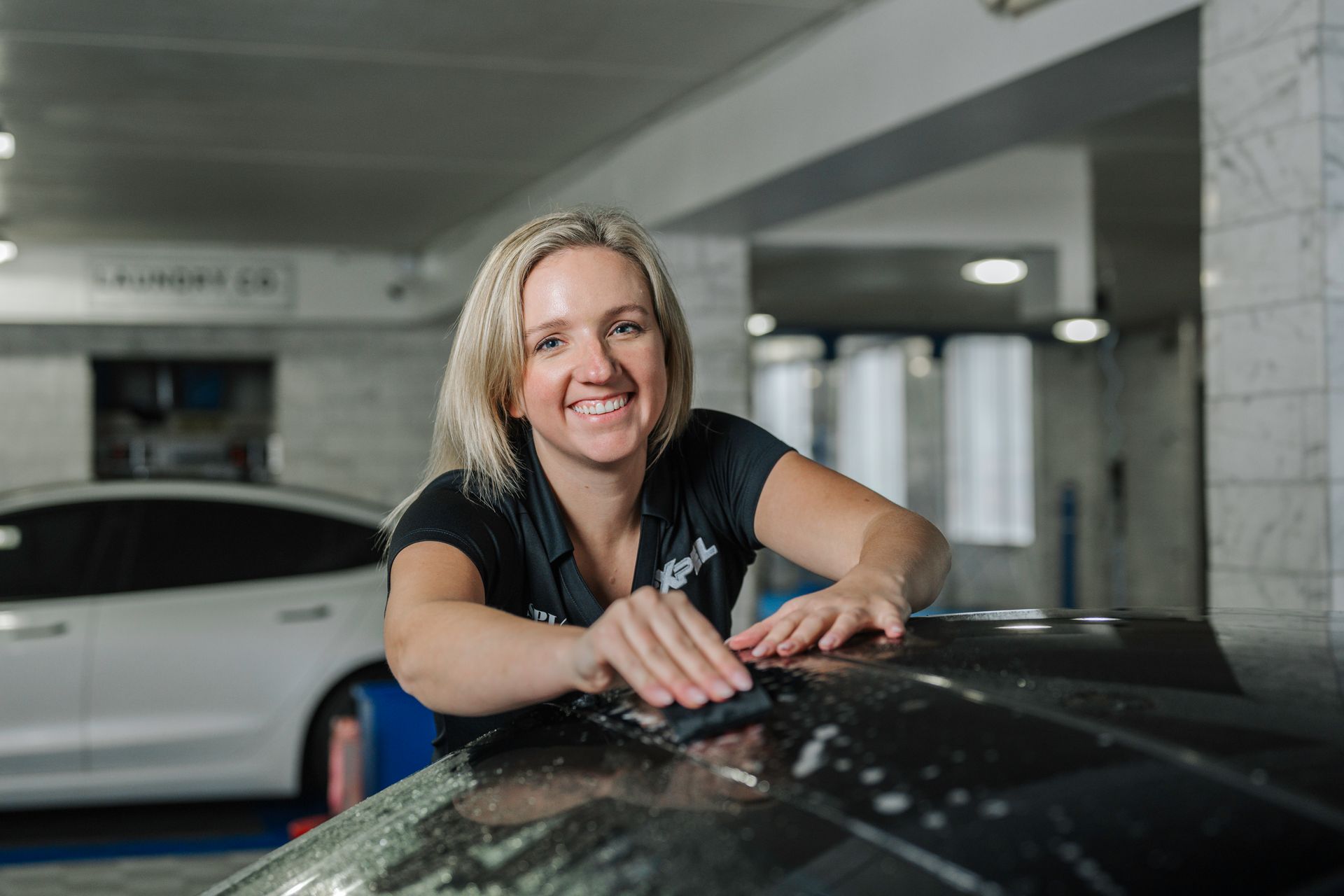 A woman is cleaning the roof of a car in a garage.
