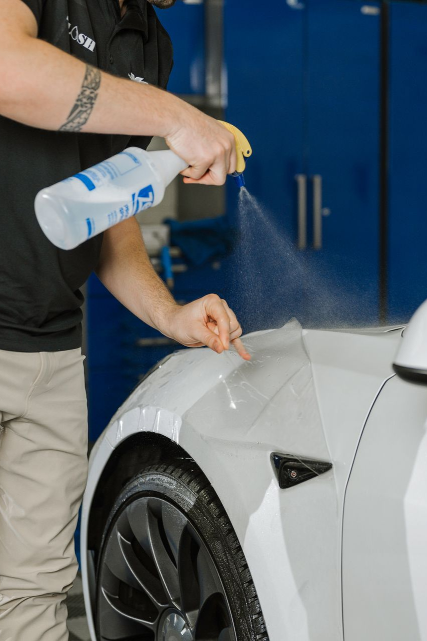 A man is spraying a protective film on the front of a white car.