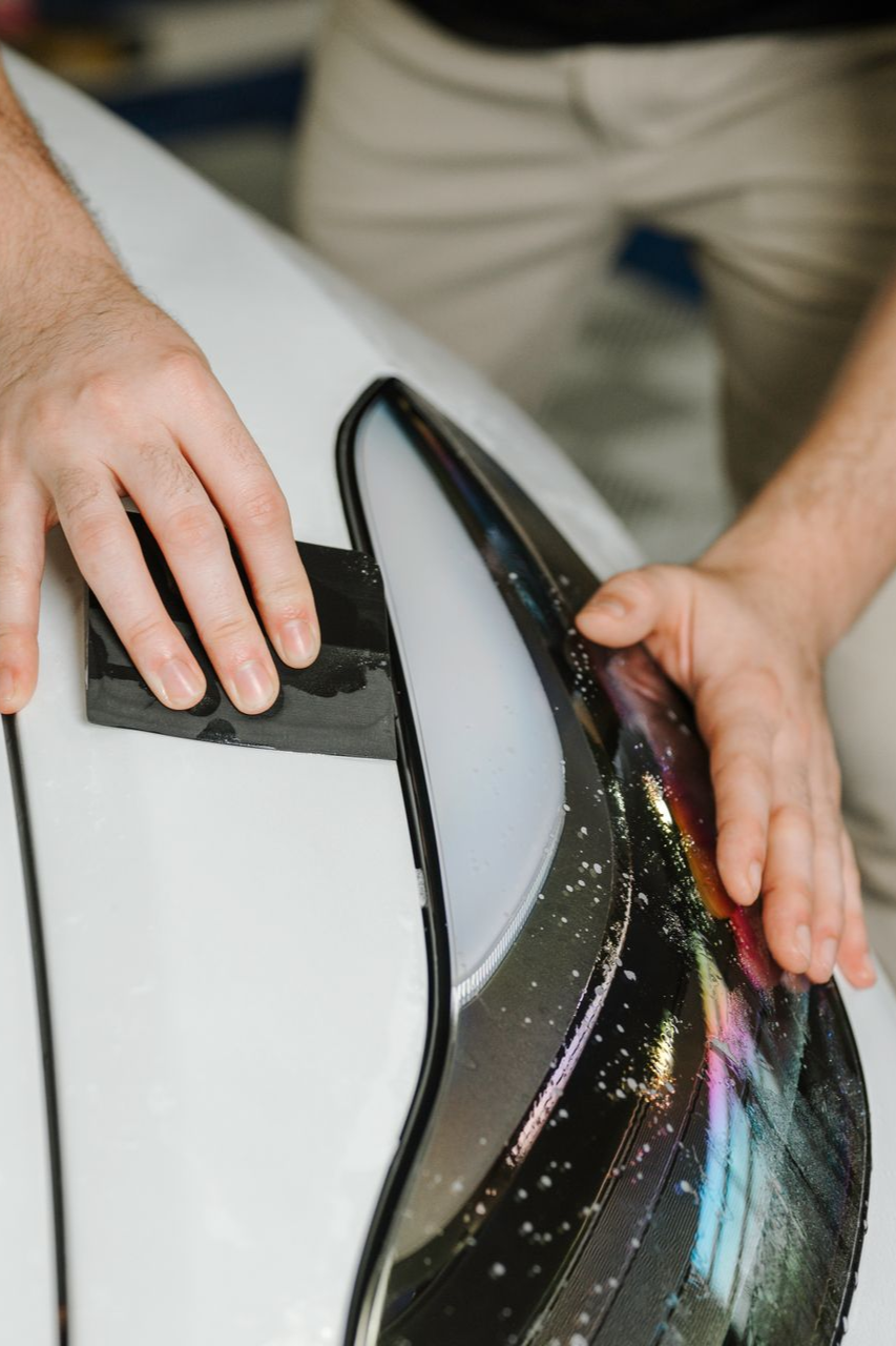 A man is polishing the headlight of a white car.