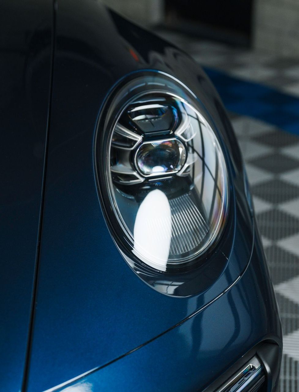 Blue Porsche car headlight close-up, reflective surface, sleek design.