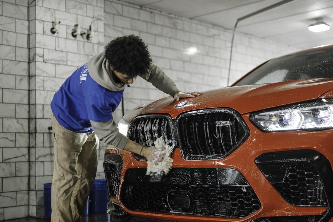 A person washing an orange BMW car in a car wash, scrubbing the front grill.