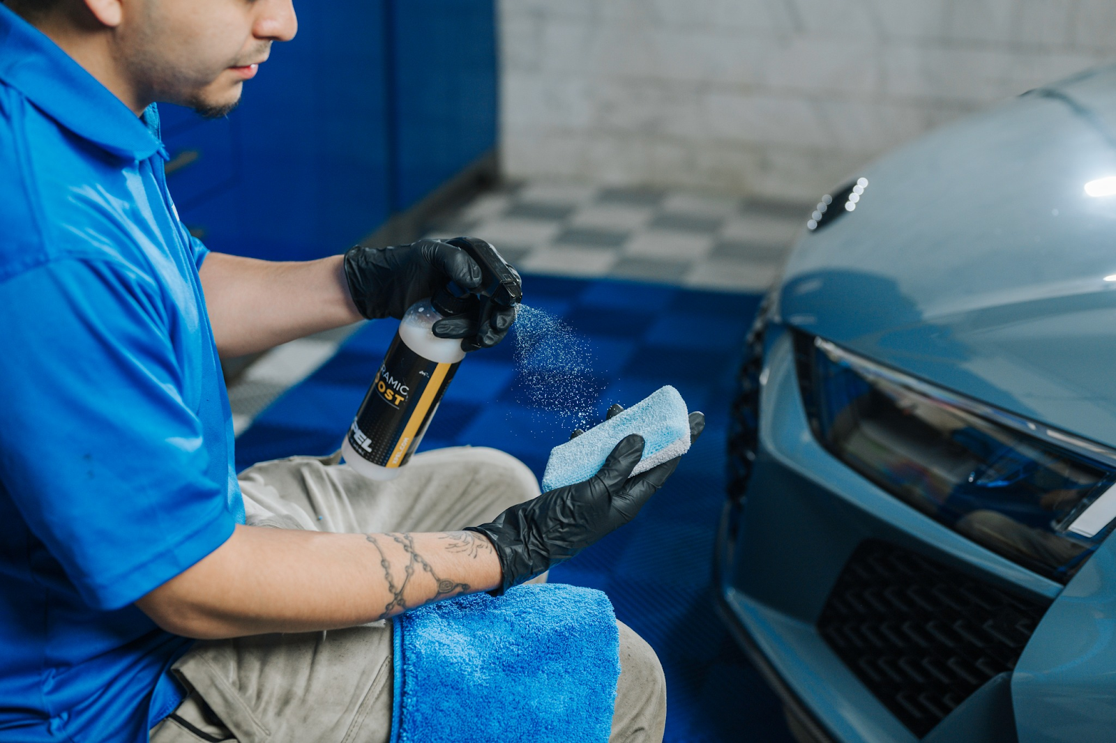 Man sprays product onto applicator, applying it to car headlight in a garage setting.
