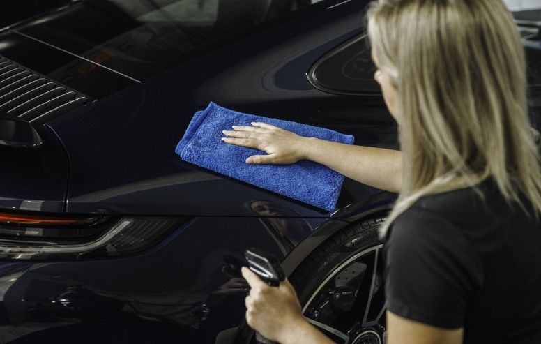 A woman is cleaning a car with a blue towel.