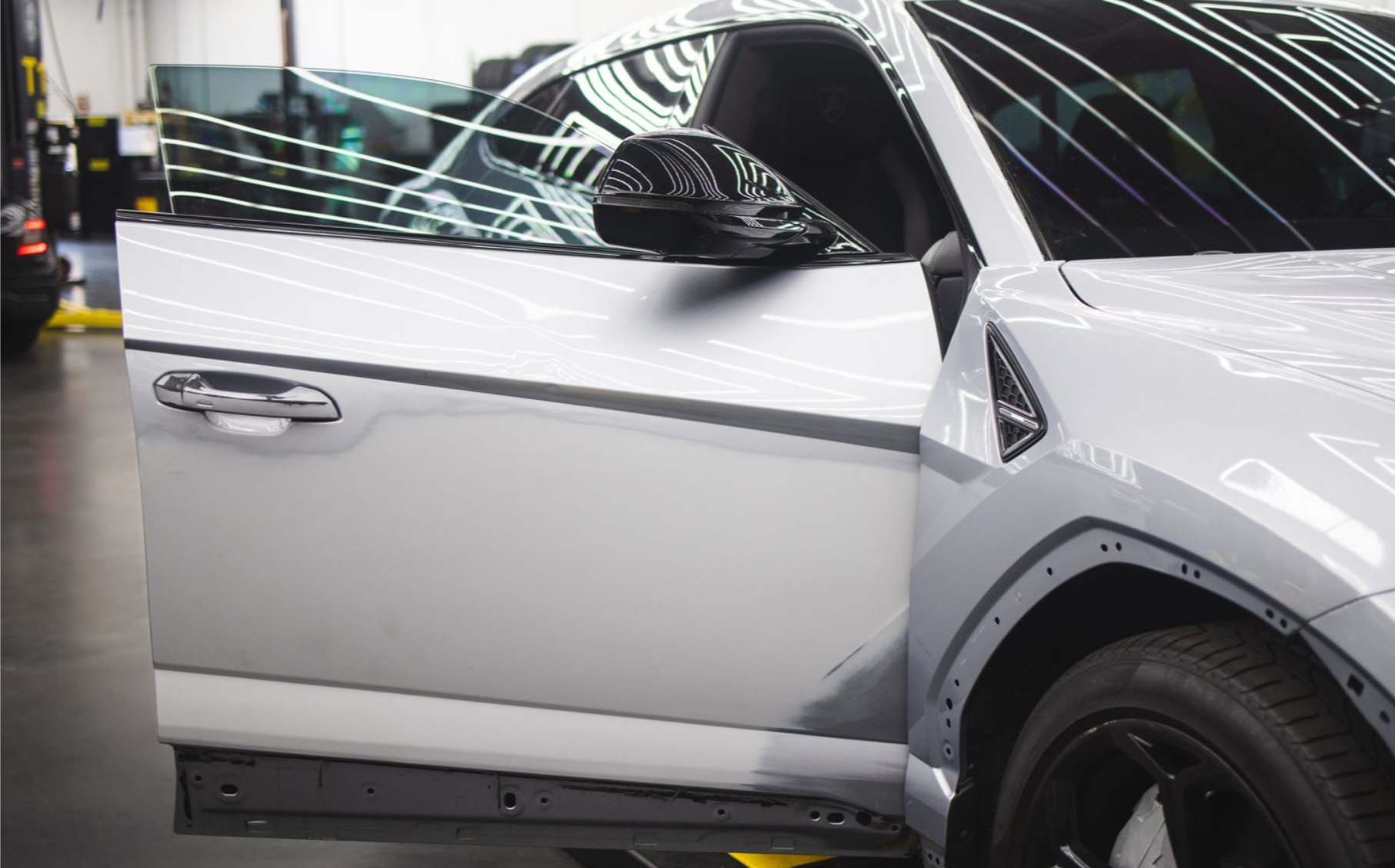 White car with driver’s door open in a garage, showing the front side and wheel.
