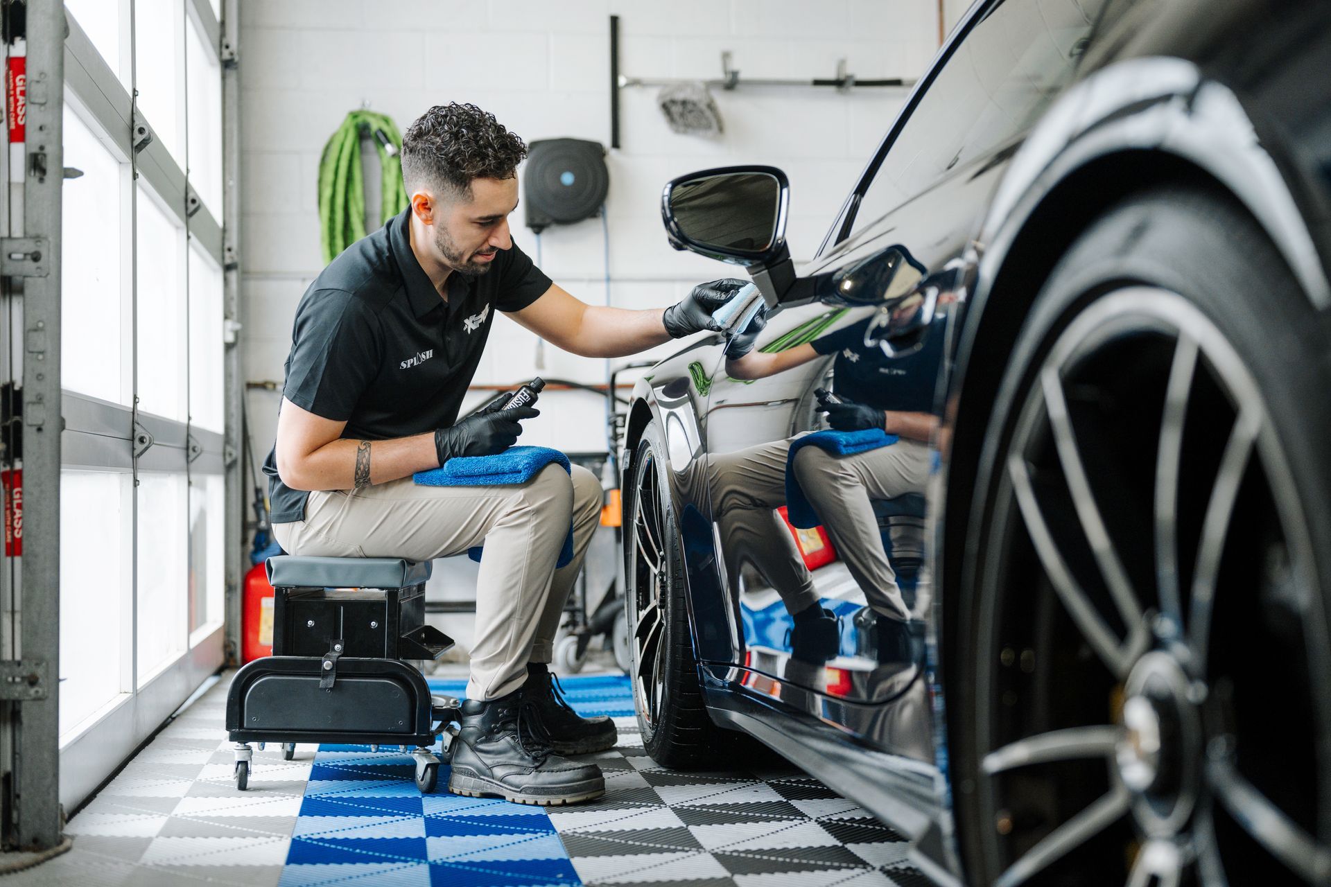 A woman is cleaning the roof of a car in a garage.