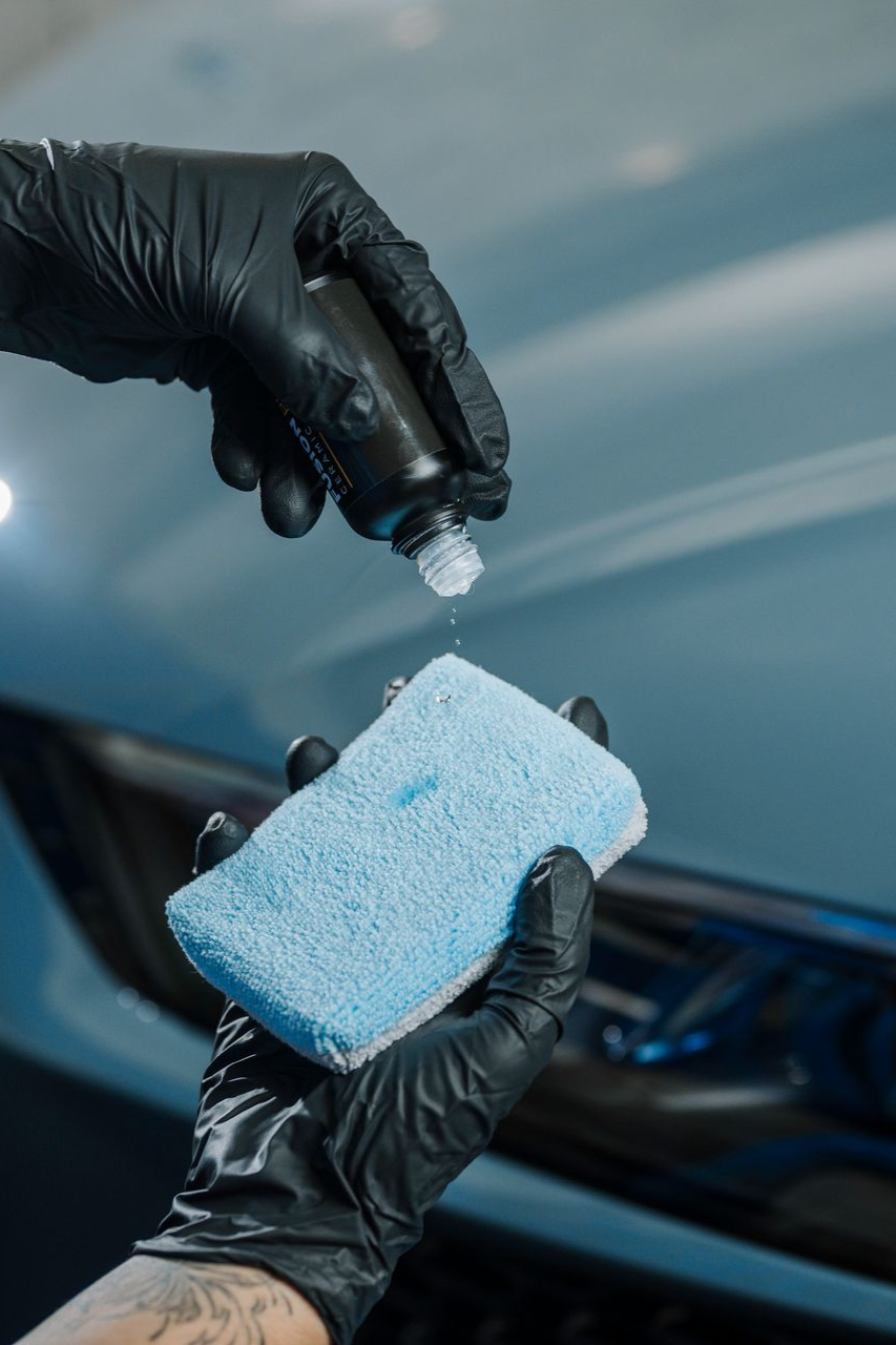 A person is cleaning a car with a sponge and a spray bottle.