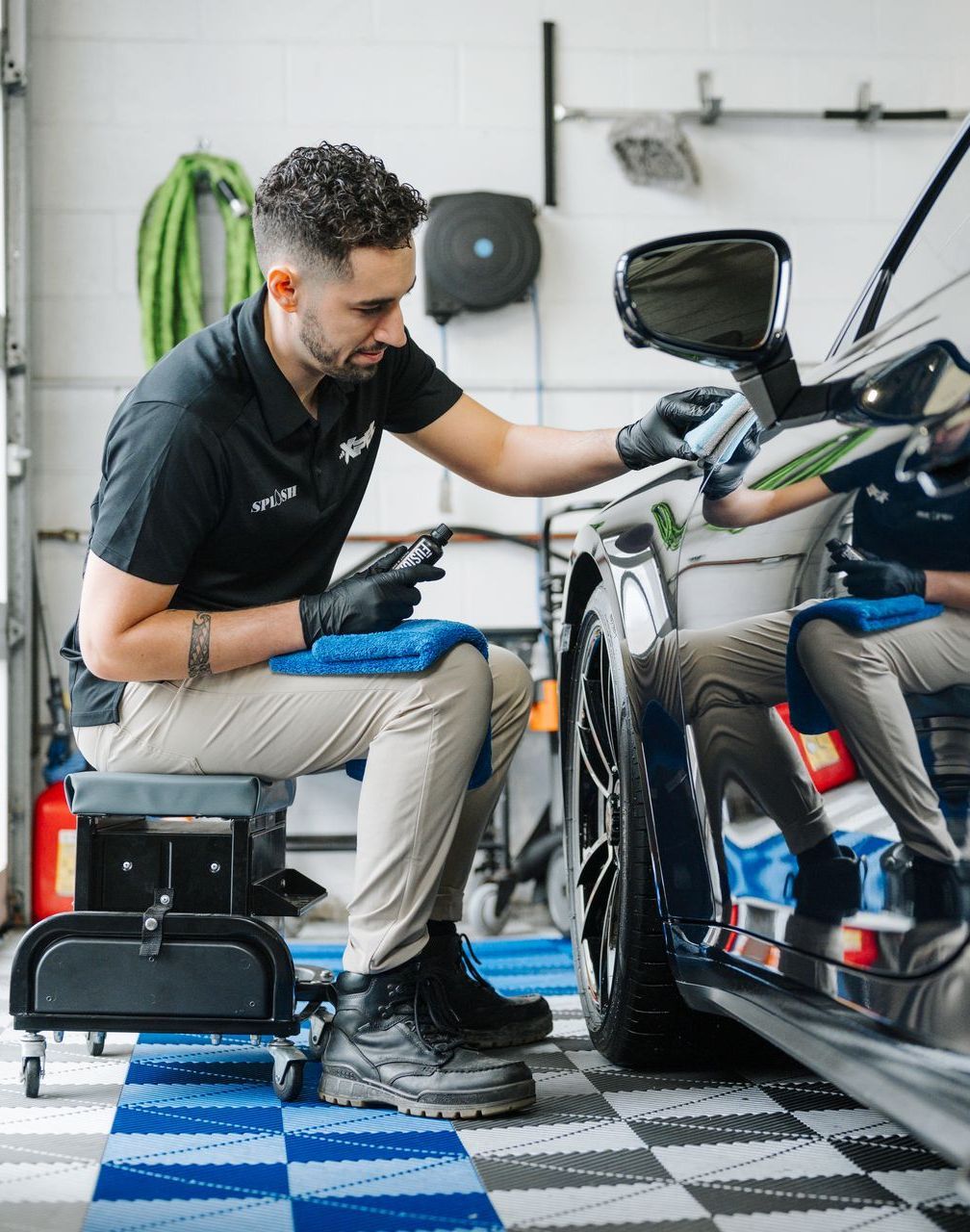 A man is sitting on a stool cleaning a car in a garage.