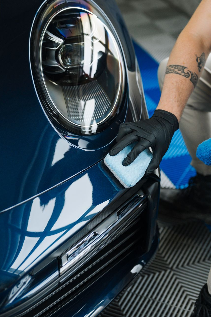 A man is polishing the front of a blue car.