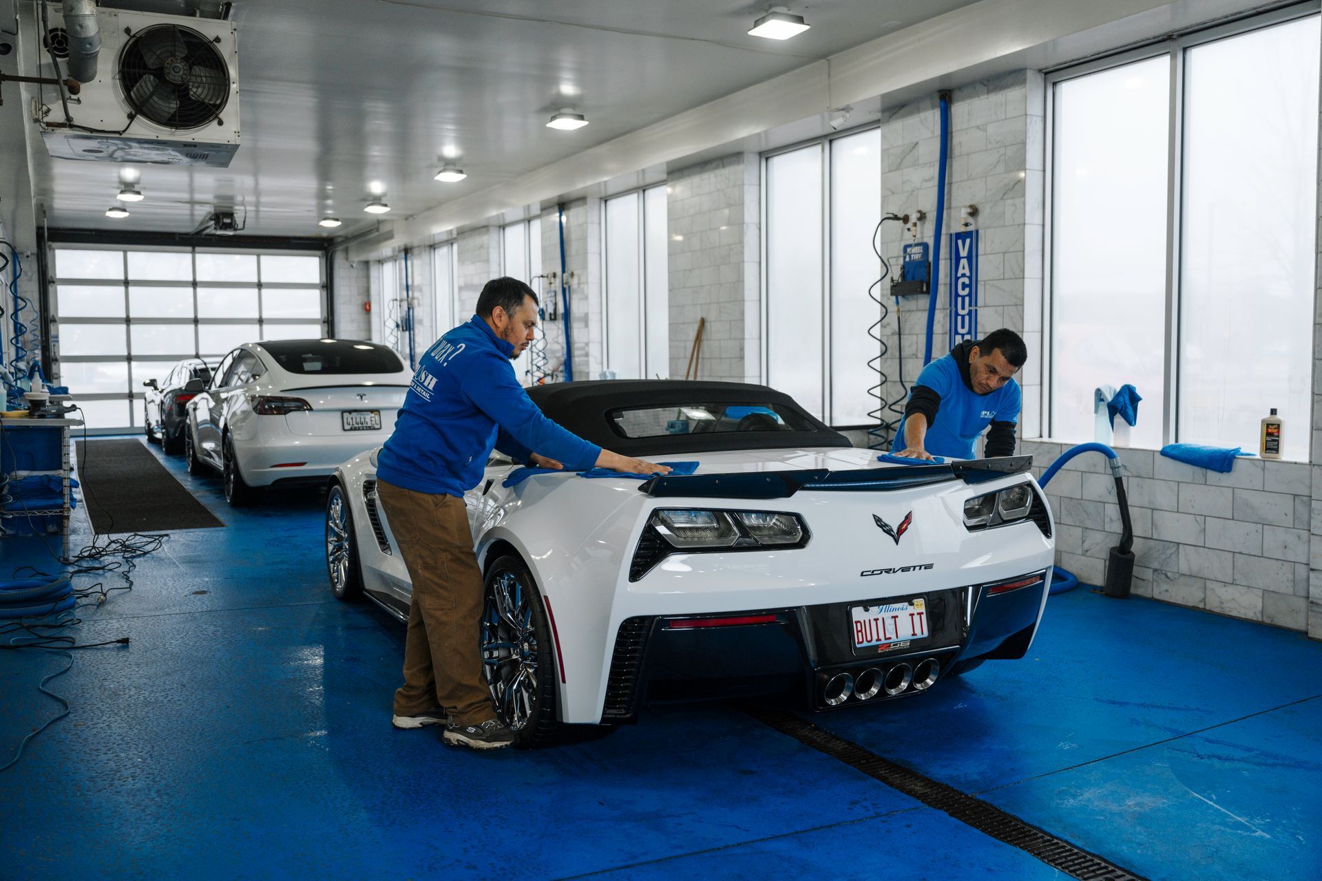 Two men are washing a white sports car in a car wash.