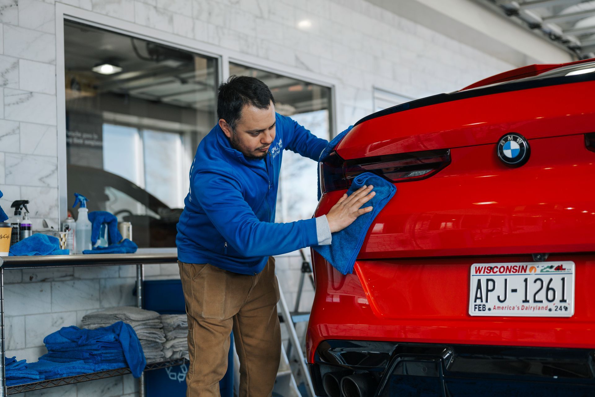 Man wiping a red BMW with a blue cloth in a car wash garage