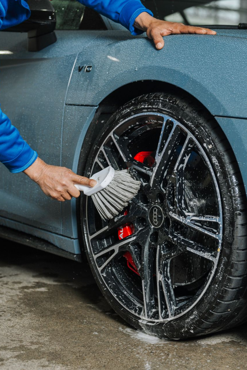 A man is cleaning the wheel of a car with a brush.