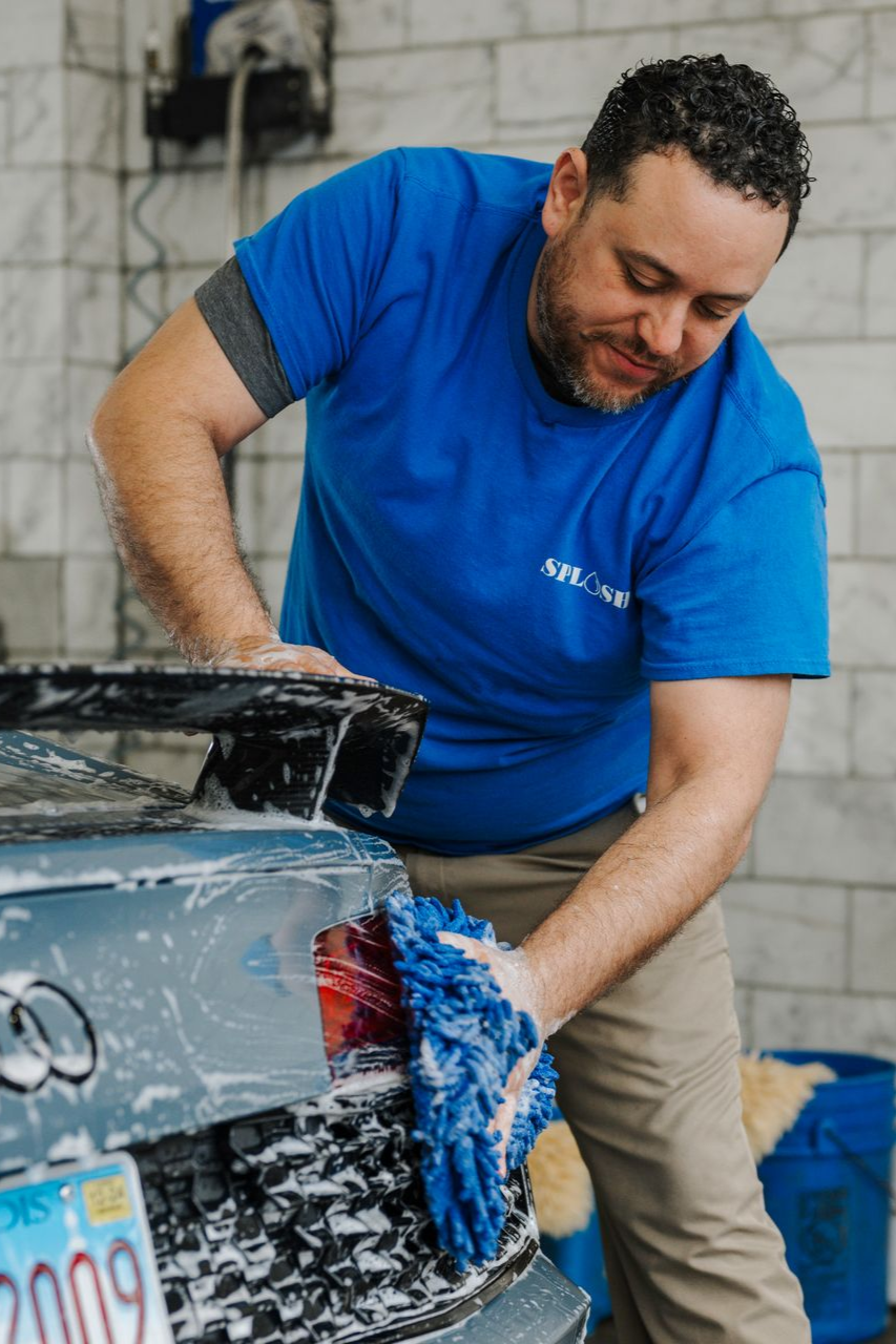 A man in a blue shirt is washing a car in a car wash.