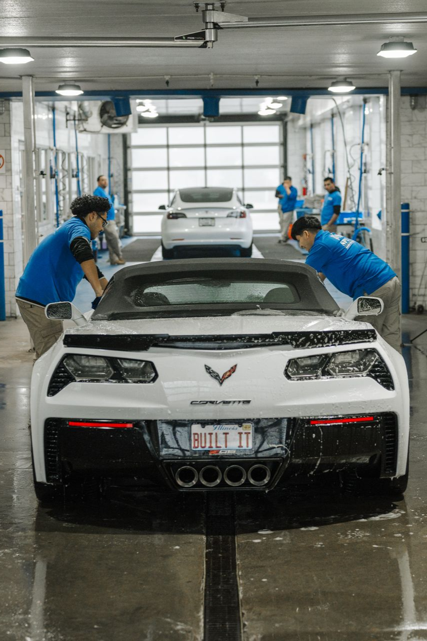 A white corvette is being washed in a car wash.
