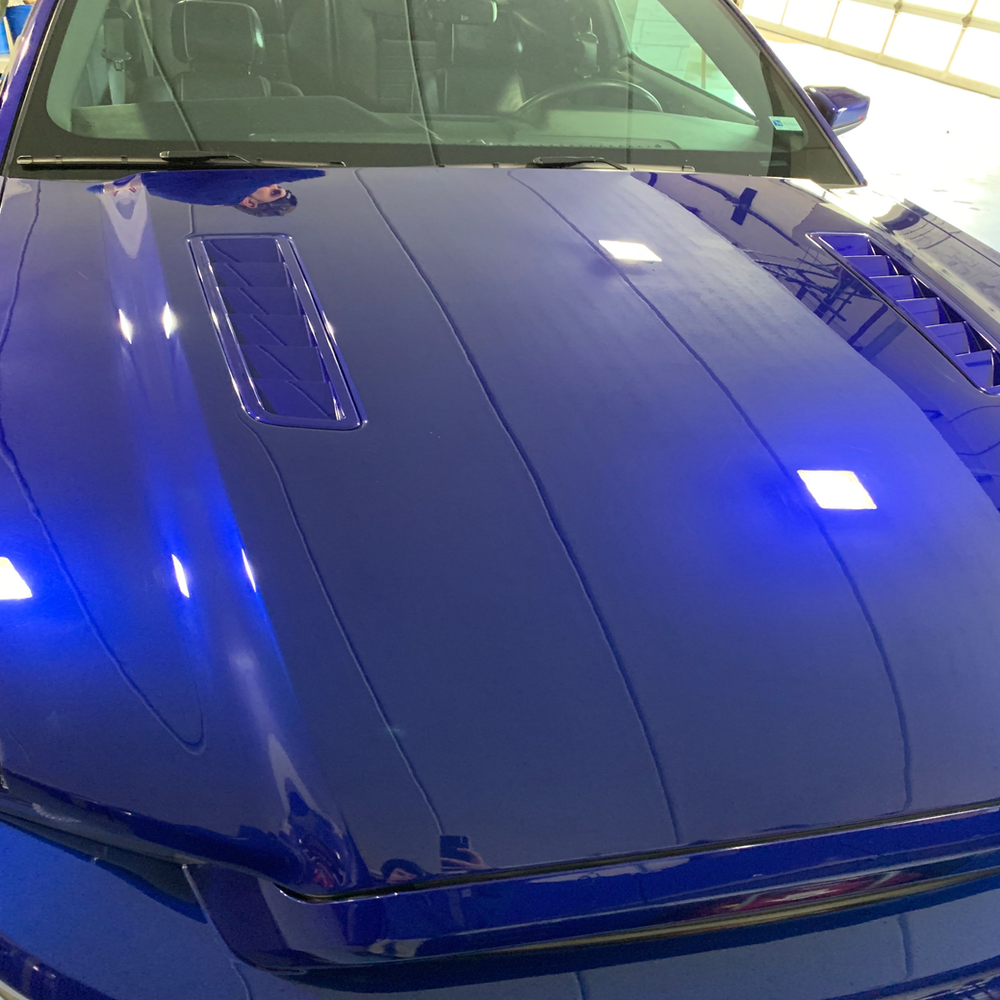 A close up of a blue car 's hood and windshield