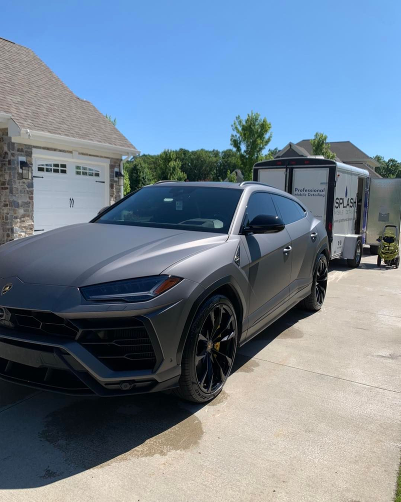 A gray car is parked in a driveway next to a trailer.