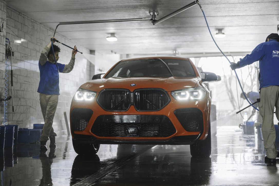 Two men are washing a red car in a garage.