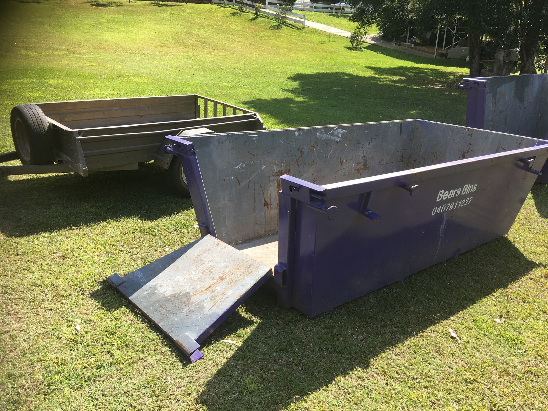 Purple Dumpster With Ramp Open, Metal Trailer, on a Grassy Field — Skip Bin Hire Sunshine Coast in Noosa, QLD