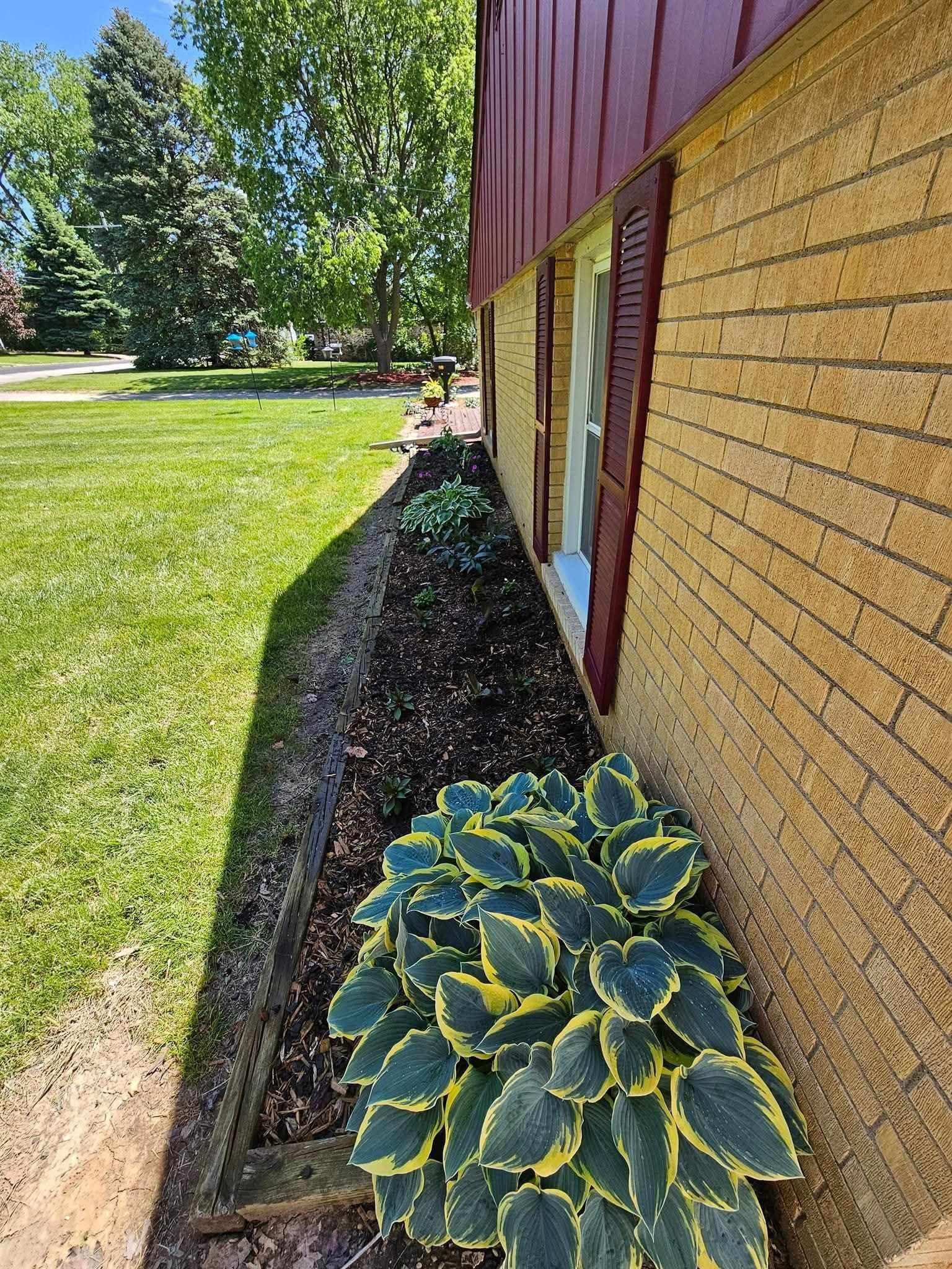 Yellow house siding with a red door and a landscaped flower bed beside a green lawn