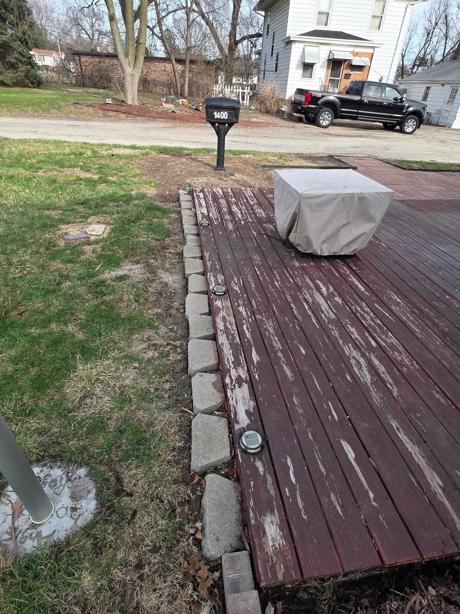 Deck with a covered object, mailbox, and yard beside a driveway and house