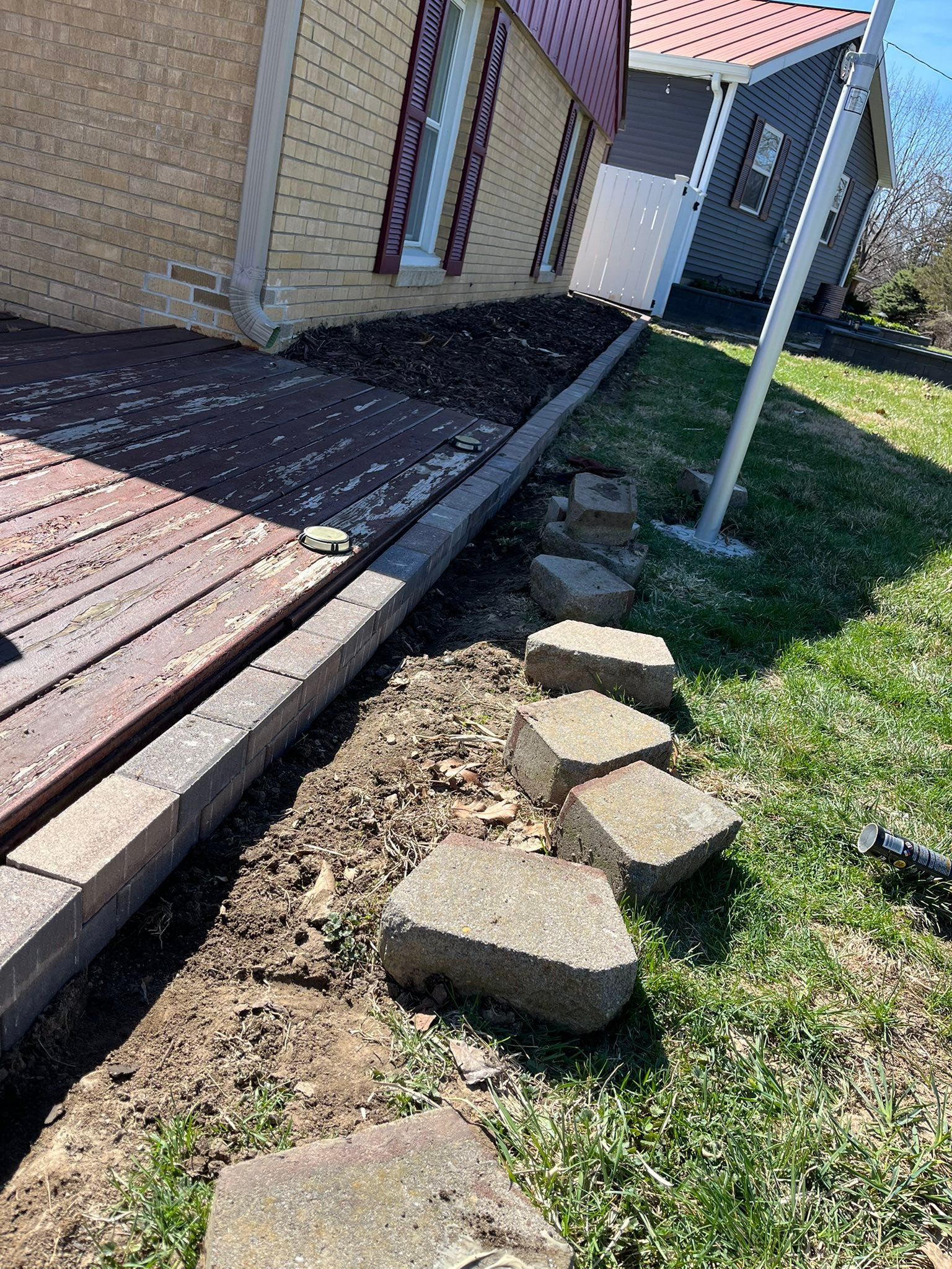 Broken stepping stones beside a house walkway and grass lawn in bright sunlight