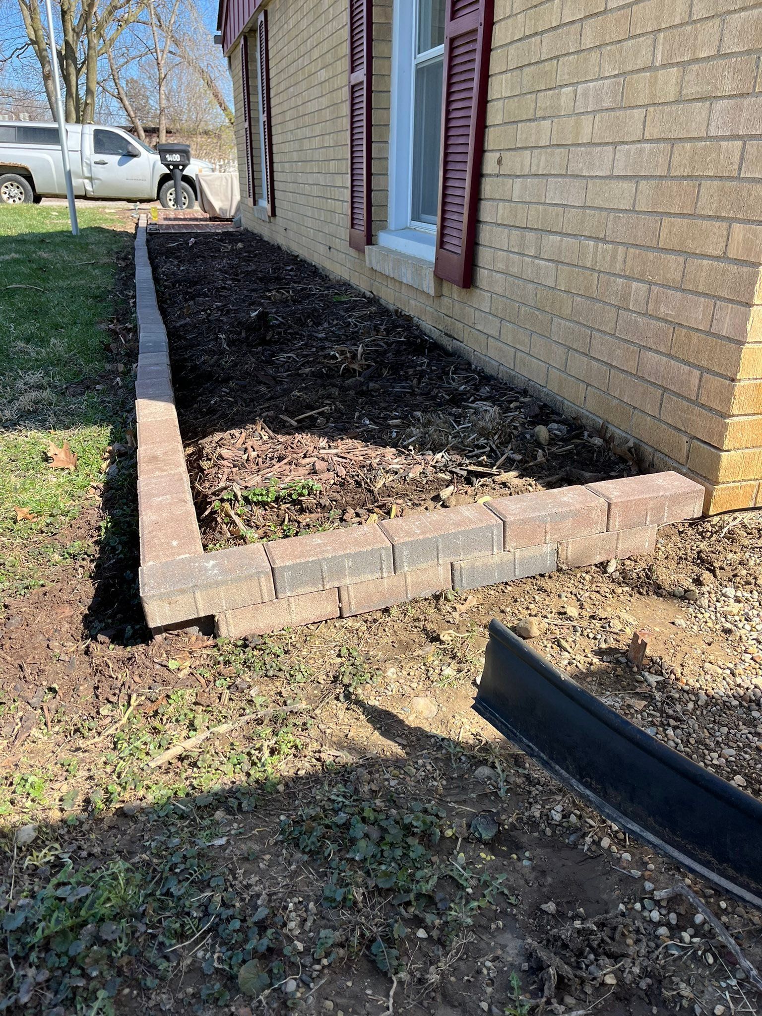 Brick house side yard with a raised mulch bed edged in bricks and a parked truck in the background