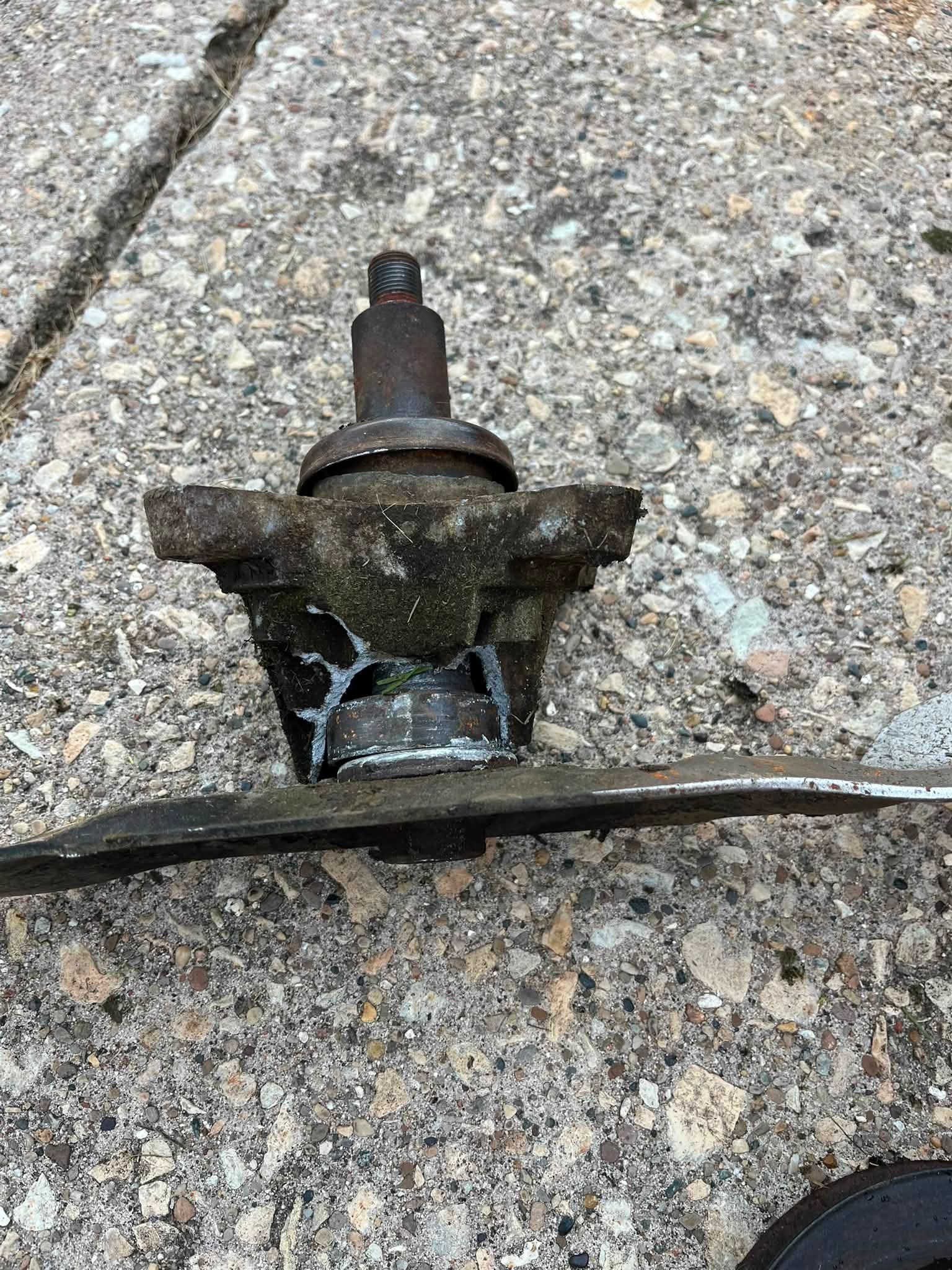 Small broken metal part with a threaded stud lying on rough gray concrete.