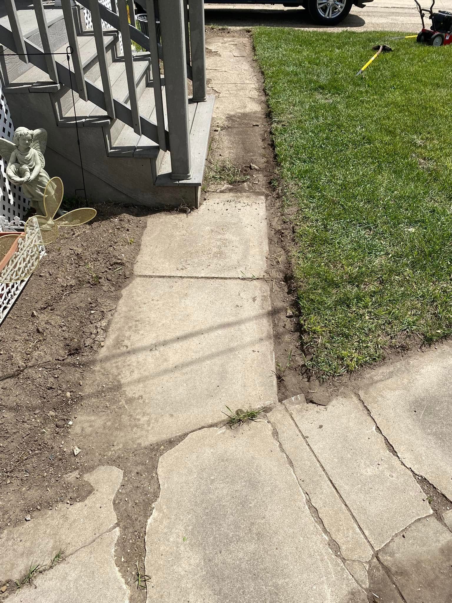 Concrete walkway beside a lawn, with porch steps and railings casting shadows