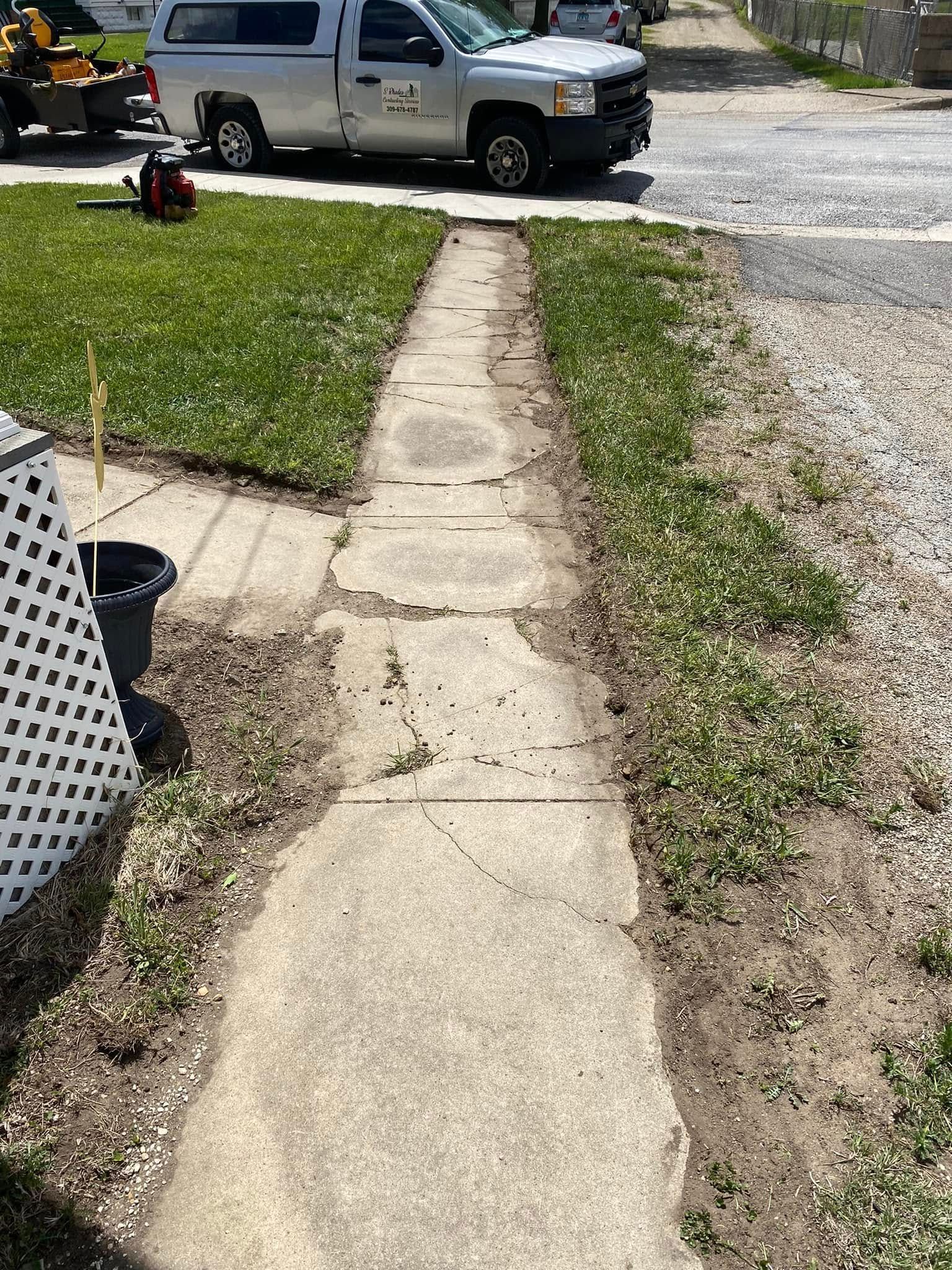 Concrete walkway leading to a gravel driveway with a silver pickup truck parked ahead
