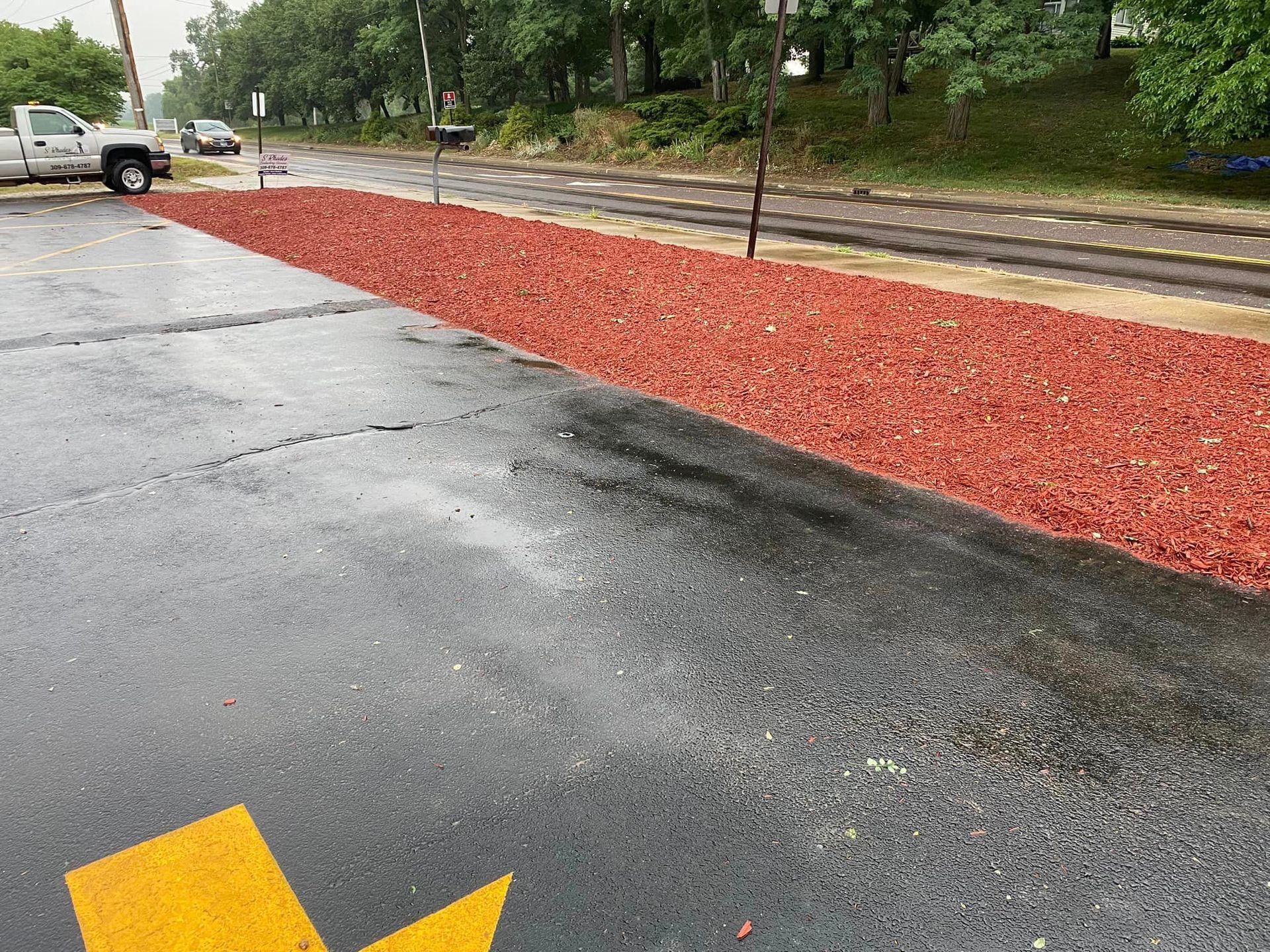 Wet parking lot beside a red mulch strip and sidewalk on a rainy day