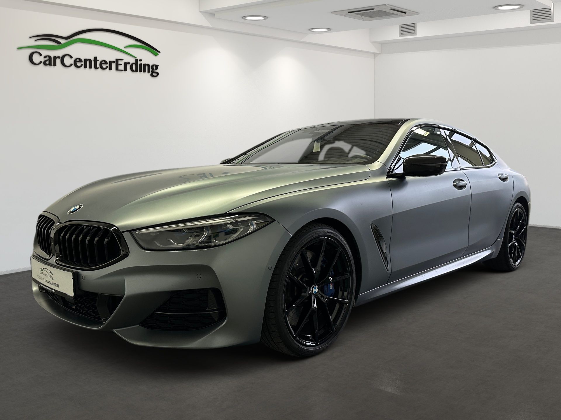 Ein silbernes BMW Coupé mit schwarzen Felgen und einem CarCenterErding-Logo an der Wand steht in einem Ausstellungsraum.