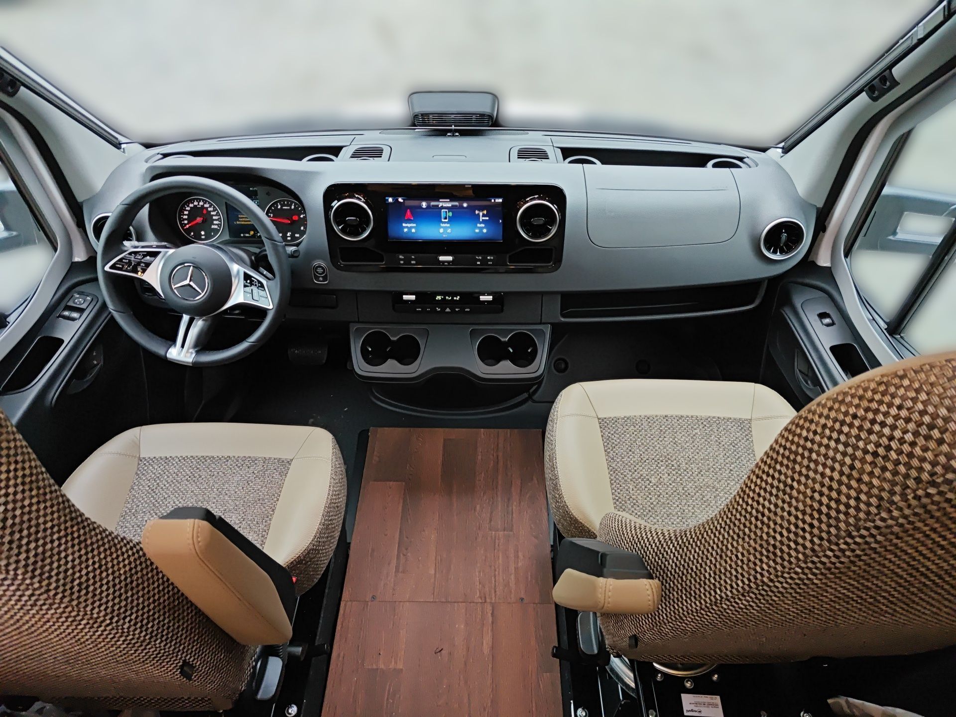 Blick von den Vordersitzen eines Lieferwagens mit Armaturenbrett, Lenkrad, Touchscreen und Holzboden.