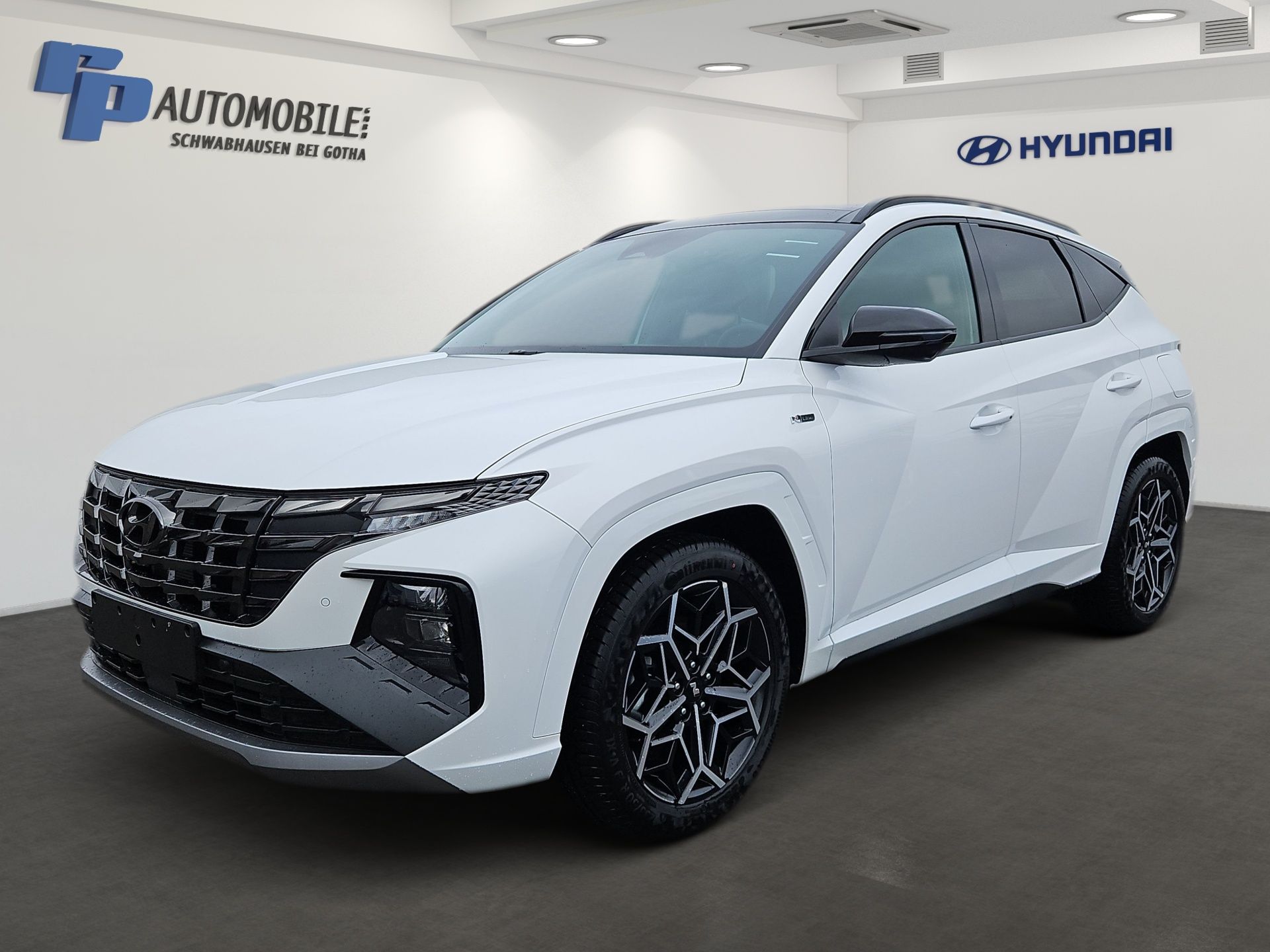 Weißer Hyundai SUV im Ausstellungsraum, schräge Frontansicht, mit schwarzen Felgen und großem schwarzen Kühlergrill.