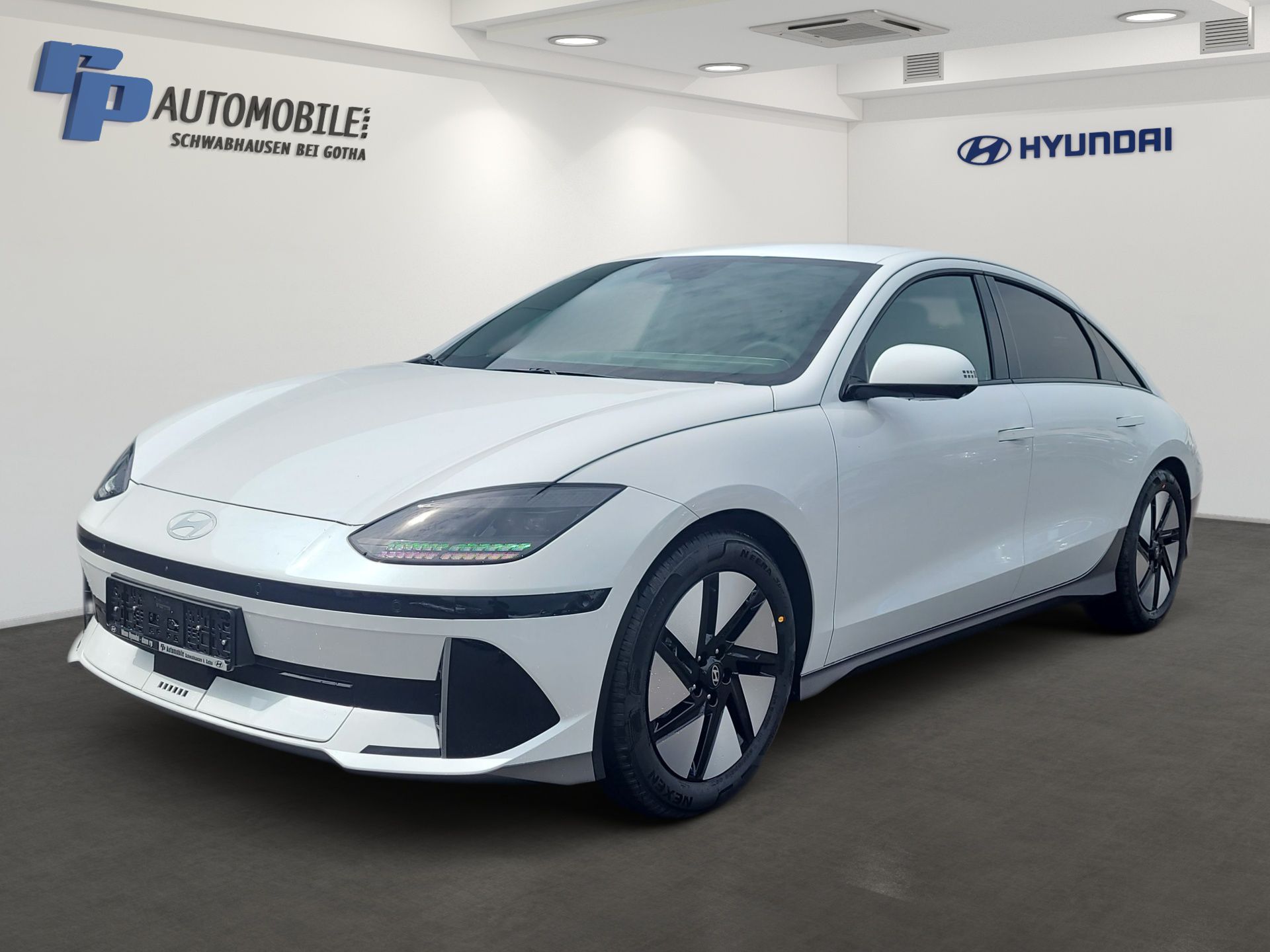 Eine weiße Hyundai-Limousine steht in einem Ausstellungsraum mit dem Autohauslogo an den Wänden.
