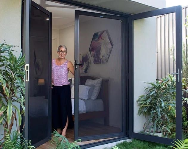 A woman is standing in front of a screen door in a bedroom.