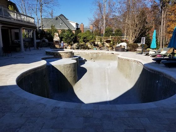 Empty backyard swimming pool with curved concrete edges and patio furniture in bright sunlight