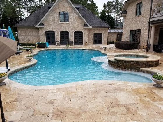 Backyard pool with tan stone patio and brick house, featuring a curved blue swimming pool and spa.