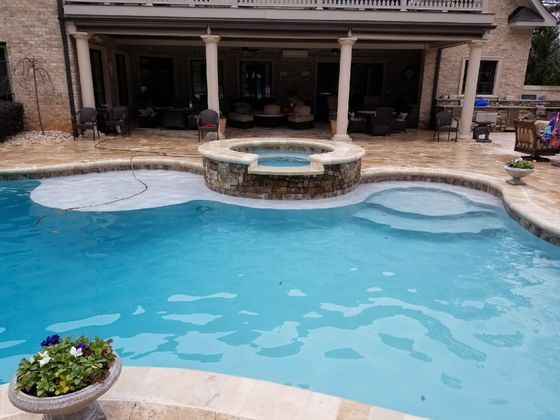 Backyard pool with spa and covered patio beside a stone house