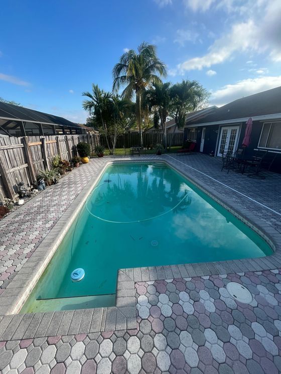 Backyard pool with turquoise water, surrounded by pavers and houses under a blue sky.