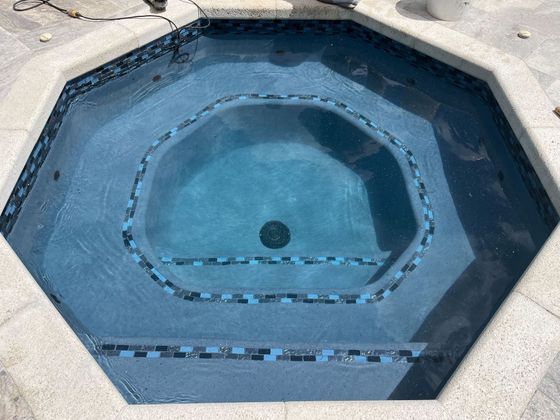 Empty blue-tiled octagonal hot tub with a single drain in the center