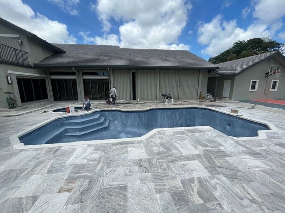 Empty backyard pool with a light gray patio and a house in the background