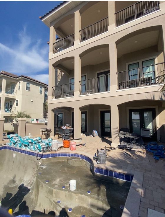 Courtyard with unfinished swimming pool beside a beige apartment building and patio chairs