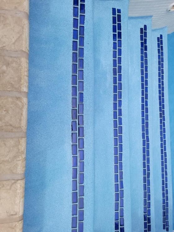 Blue swimming pool with narrow dark-blue tile stripes and tan deck at left