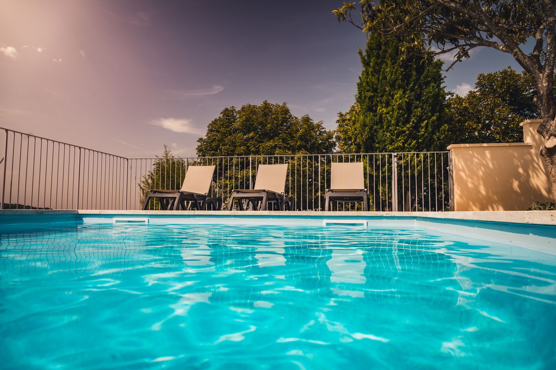 Backyard swimming pool with lounge chairs, stone patio, and flower pots beside a modern house