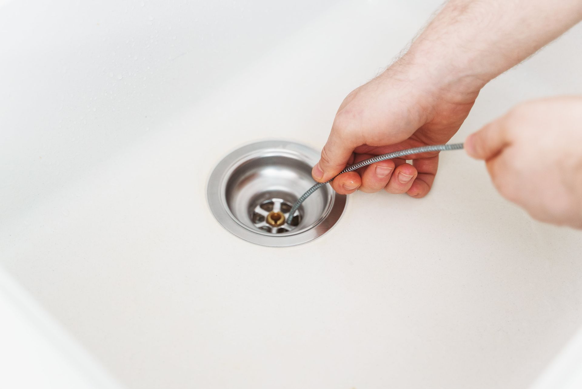 Hands using a drain cleaning tool in a white sink basin